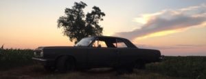 Vintage car parked in field at golden hour sunset